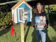 Sydney Bachert standing next to little library with a stack of books